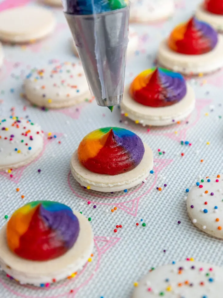 image of rainbow macarons being filled with rainbow buttercream frosting