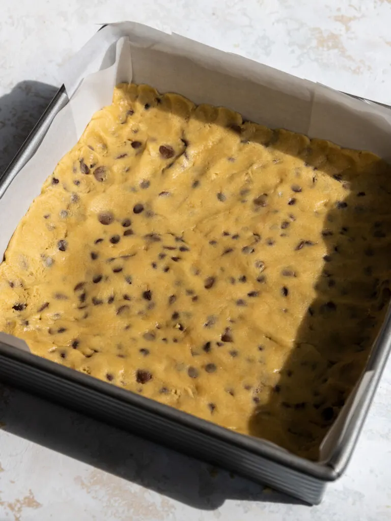 image of a layer of cookie dough being pressed into a square baking pan