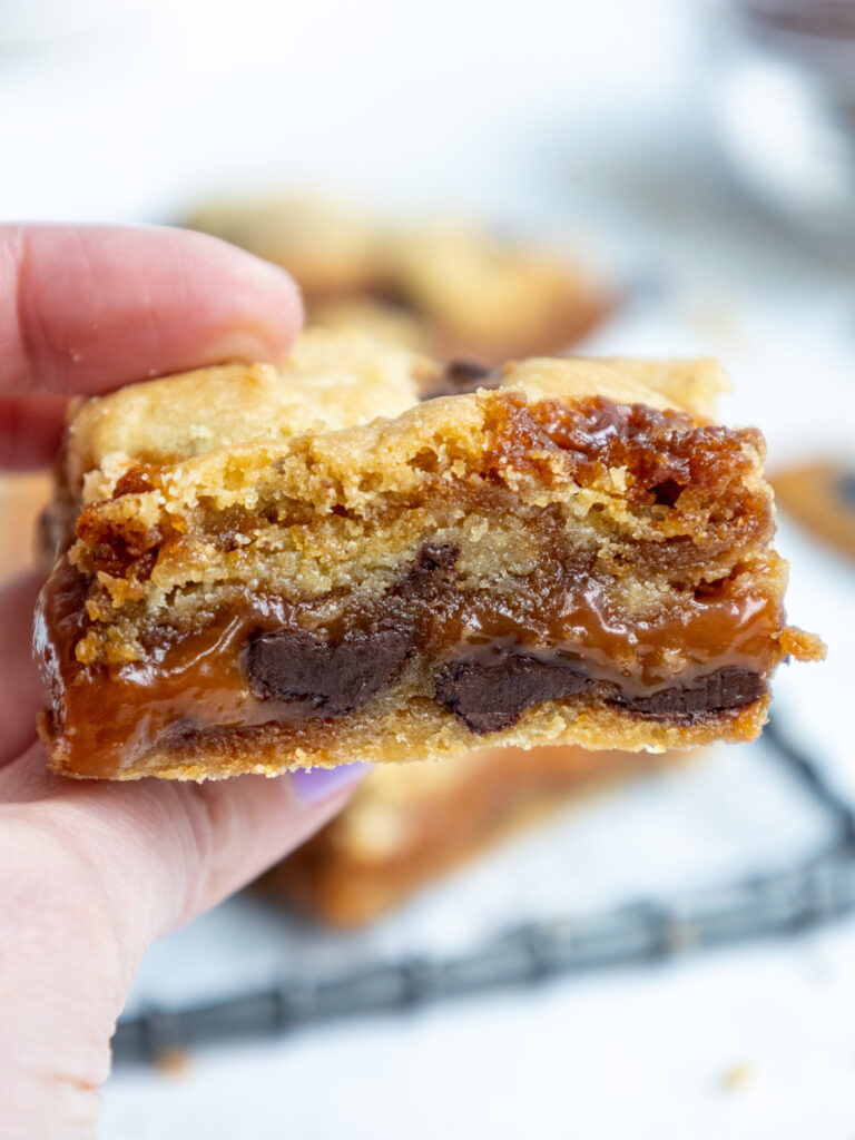 image of a caramel cookie bar being held up to show its thick layer of caramel filling