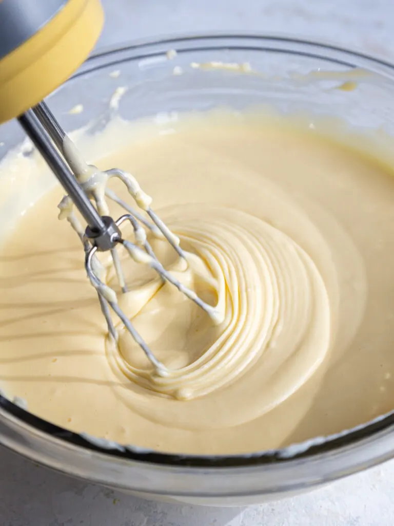 image of eggs being mixed into cheesecake batter with a hand mixer