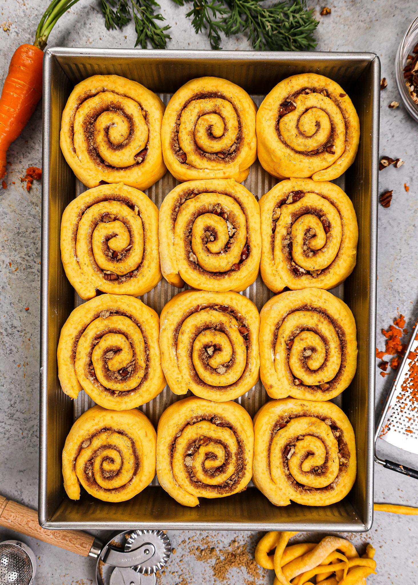 image of an overhead shot of carrot cake cinnamon rolls that have been proofed in a 9 by 13 inch pan and are ready to be baked