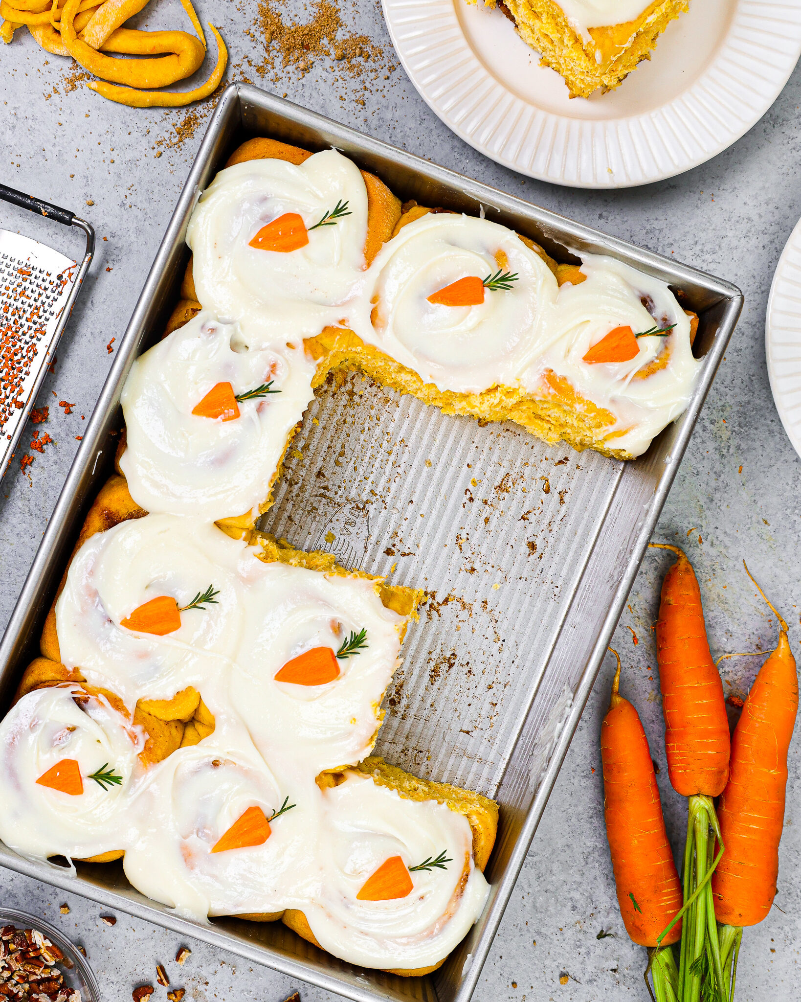 image of carrot cake cinnamon rolls in a pan that have been frosted with cream cheese frosting and decorated with cute little carrots