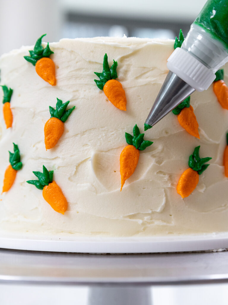 image of carrots being piped onto a 6 inch carrot cake to decorate it