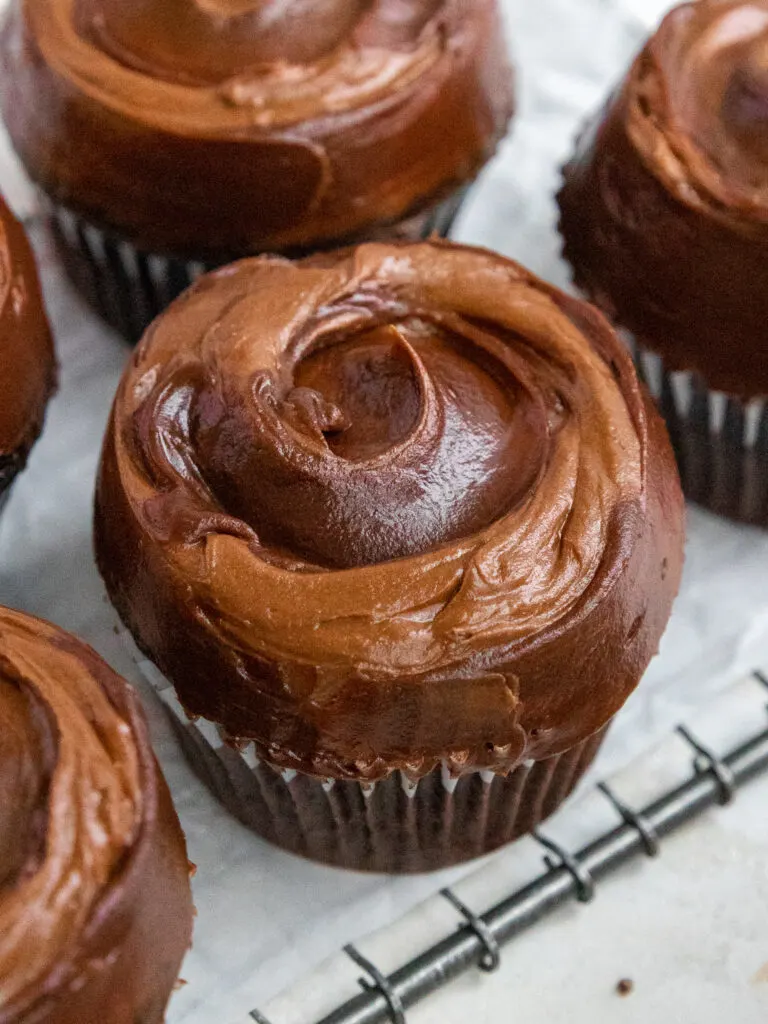 image of death by chocolate cupcakes that have been frosted with chocolate buttercream and chocolate ganache and are sitting on a wire rack lined with parchment paper