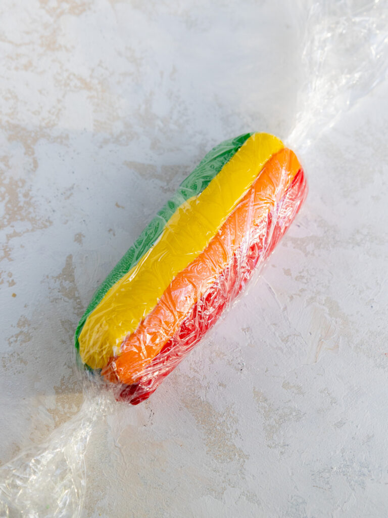 image of a rainbow frosting log that's been rolled up in plastic wrap to make rainbow swirl buttercream frosting