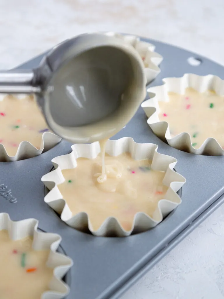 image of funfetti cupcake batter being scooped into cupcake liners
