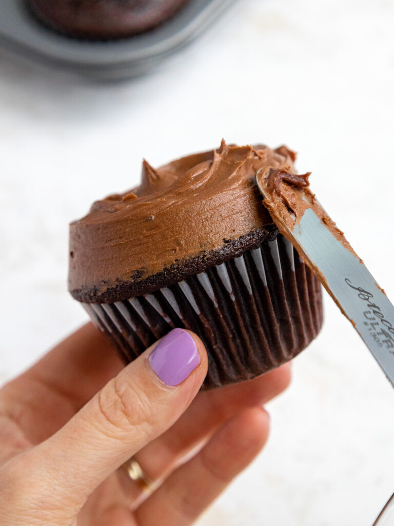 image of chocolate buttercream being smoothed onto a dark chocolate cupcake with a small offset spatula