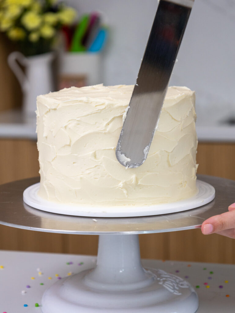 image of a small, 6 inch carrot cake being frosted with cream cheese frosting and a large offset spatula