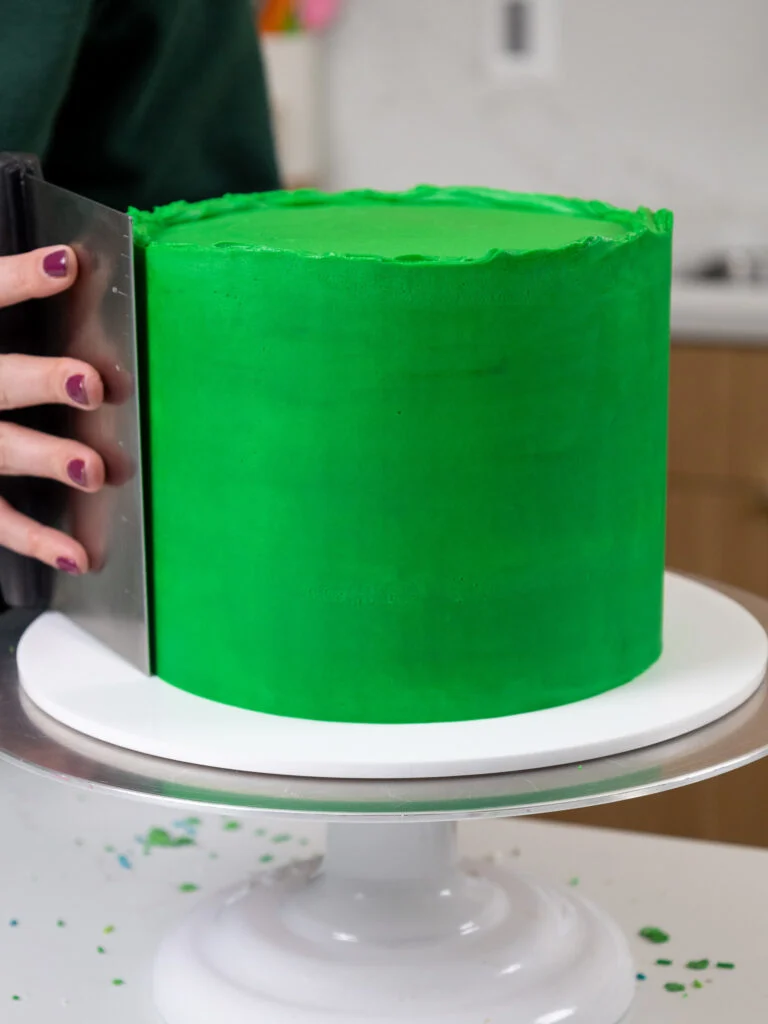 image of green buttercream being smoothed onto a layer cake to make a green drip cake