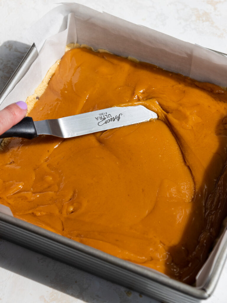 image of caramel being spread on top of a layer of cookie dough with a small offset spatula