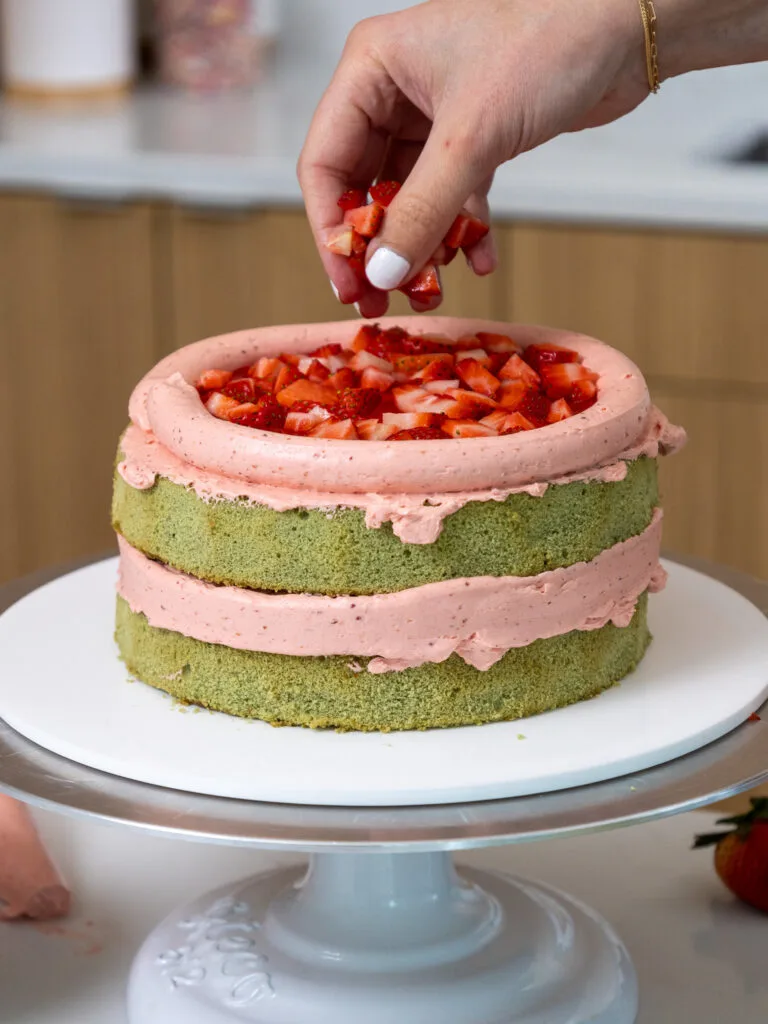 image of diced strawberries being added between the layers of a strawberry matcha cake