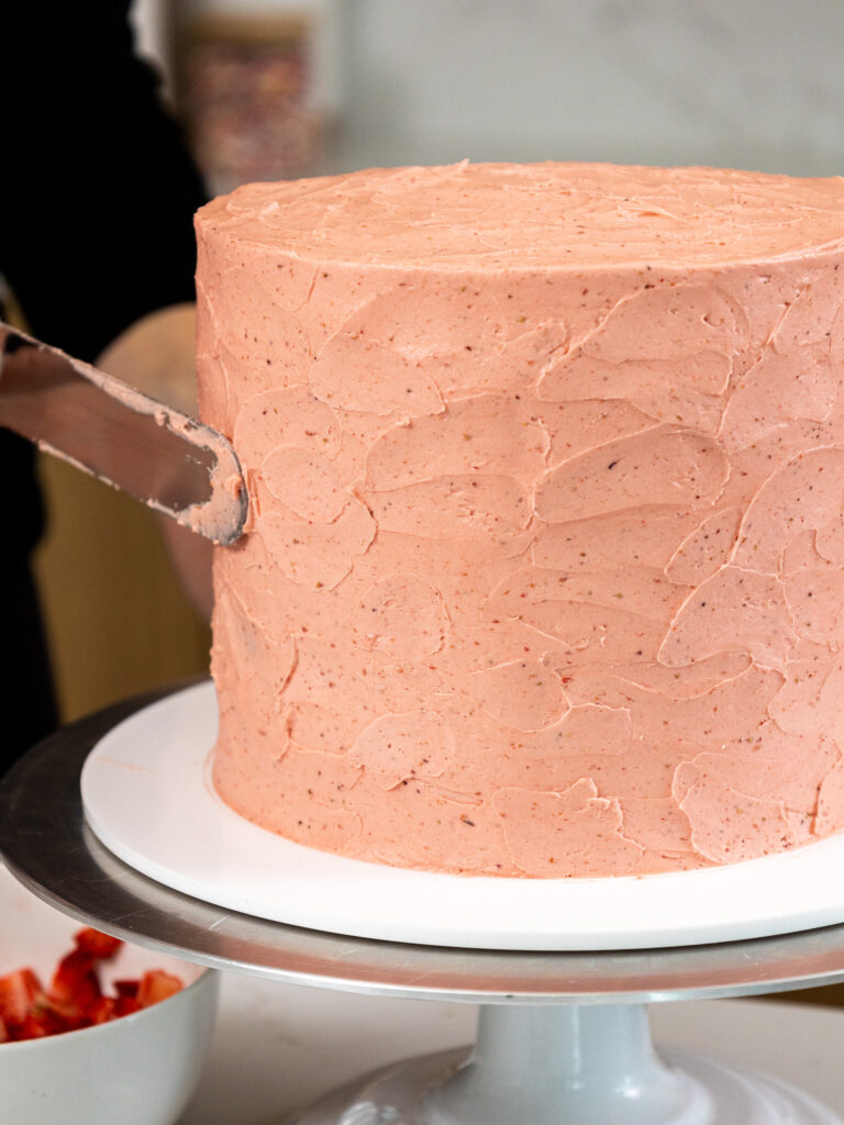 image of a cake being covered in strawberry swiss meringue buttercream to give it a textured look