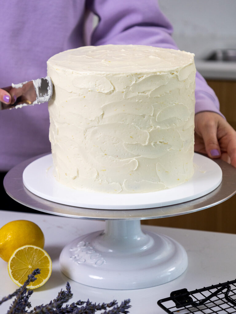 image of frosting being spread around a cake with a large offset spatula to give it a textured look
