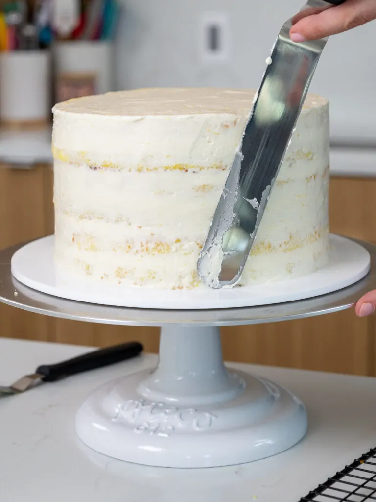 image of a lemon cake being crumb coated with Swiss meringue buttercream and a large offset spatula