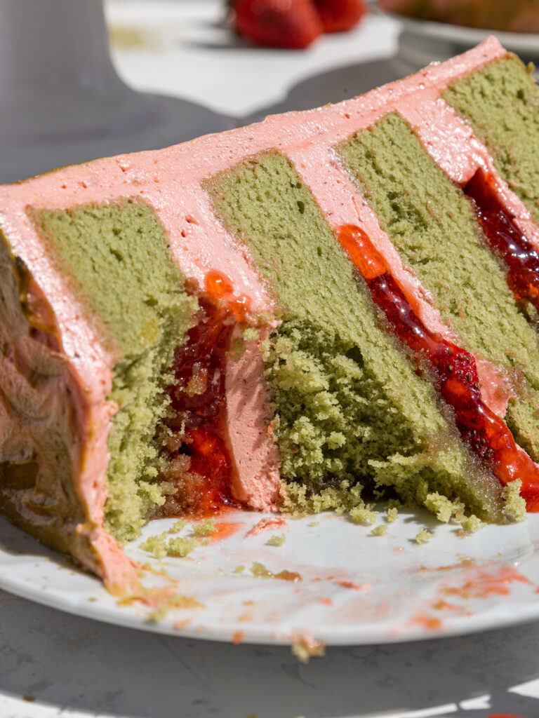 image of a slice of strawberry matcha cake on a plate that's been filled with strawberry buttercream and diced strawberries