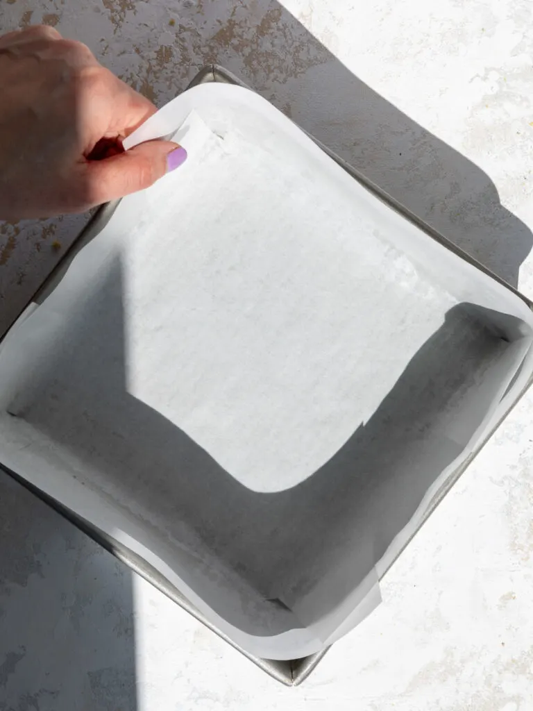 image of an 8-inch square pan being lined with parchment paper