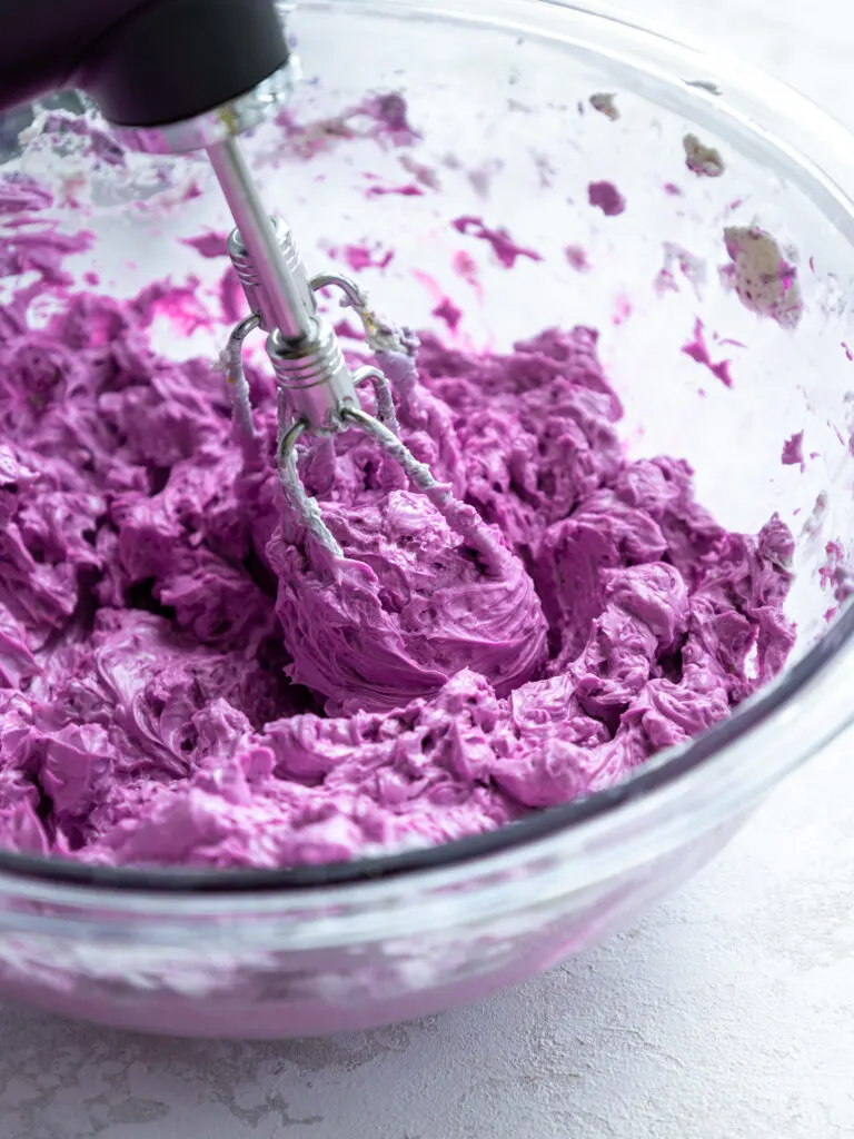 image of lavender Swiss meringue buttercream being mixed in a glass bowl with a hand mixer
