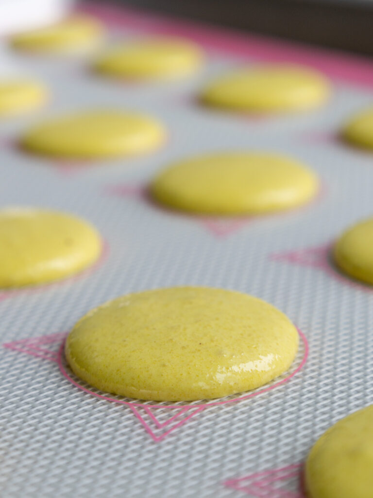 image of light yellow macaron shells that have been piped on a silpat mat and are resting before being baked