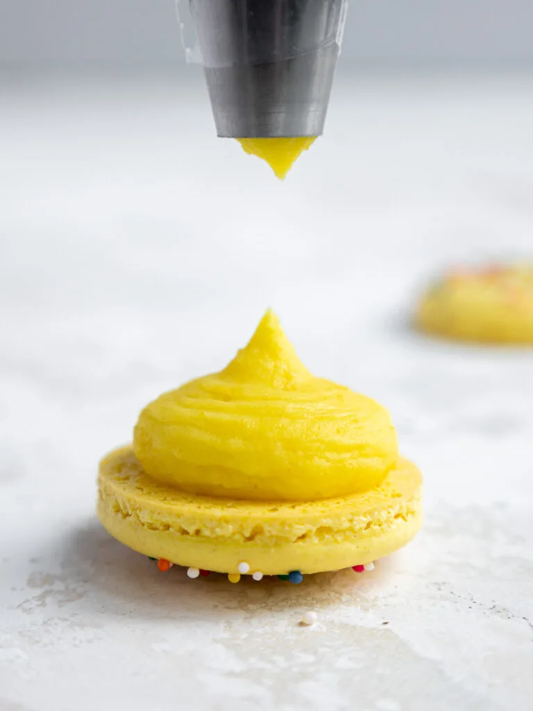 image of lemon ganache being piped onto a yellow macaron shell