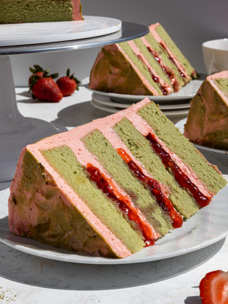 image of a slice of strawberry matcha cake on a plate that's been filled with strawberry buttercream and diced strawberries