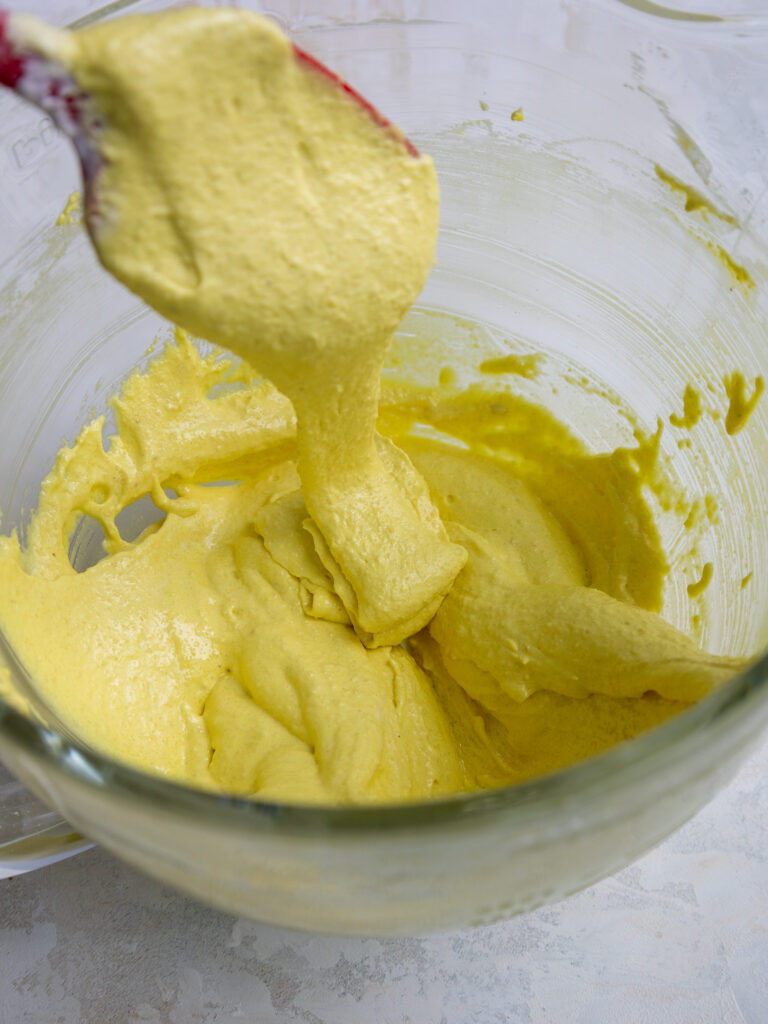 image of light yellow macaron batter that's been mixed the right amount and is falling off the rubber spatula when lifted in thick ribbons