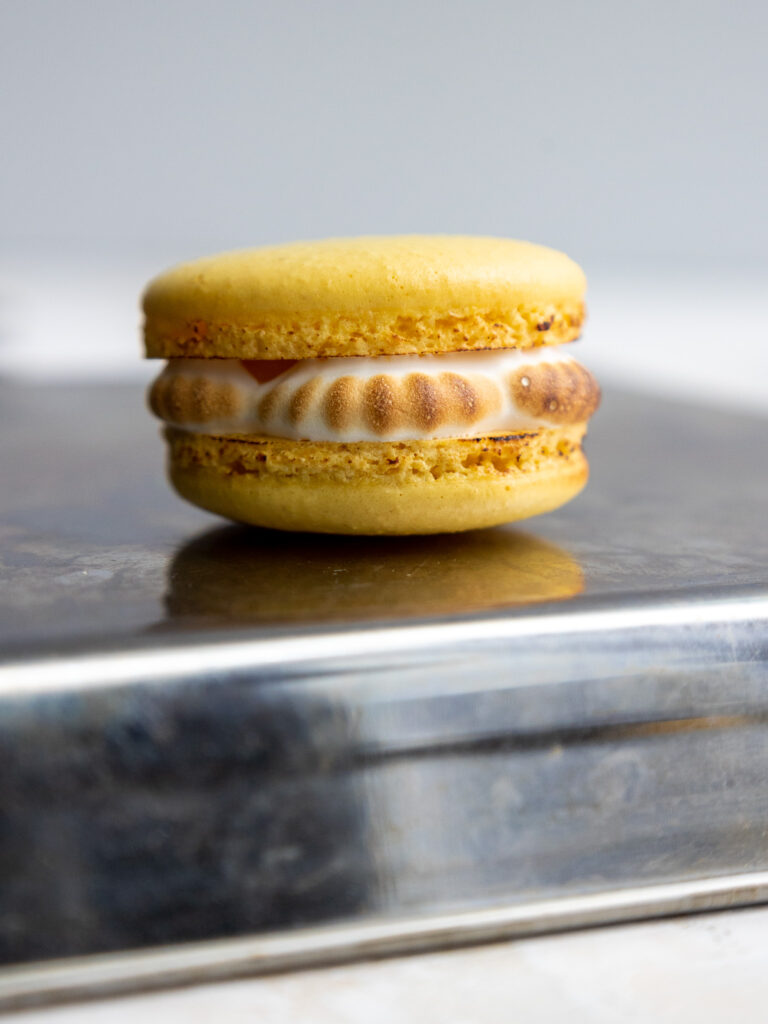 image of a lemon meringue macaron that's had the meringue filling toasted with a small kitchen torch