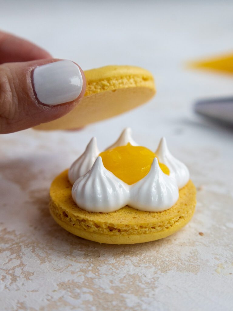 image of a lemon meringue macaron being filled with swiss meringue and lemon curd