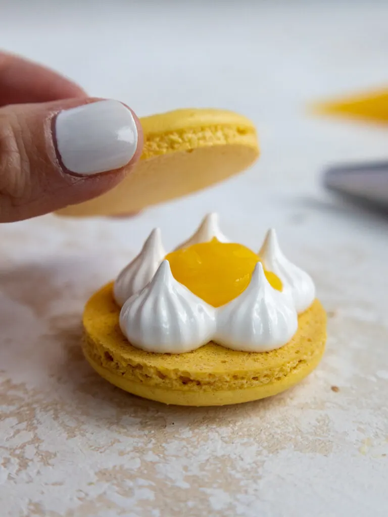 image of a lemon meringue macaron being filled with swiss meringue and lemon curd