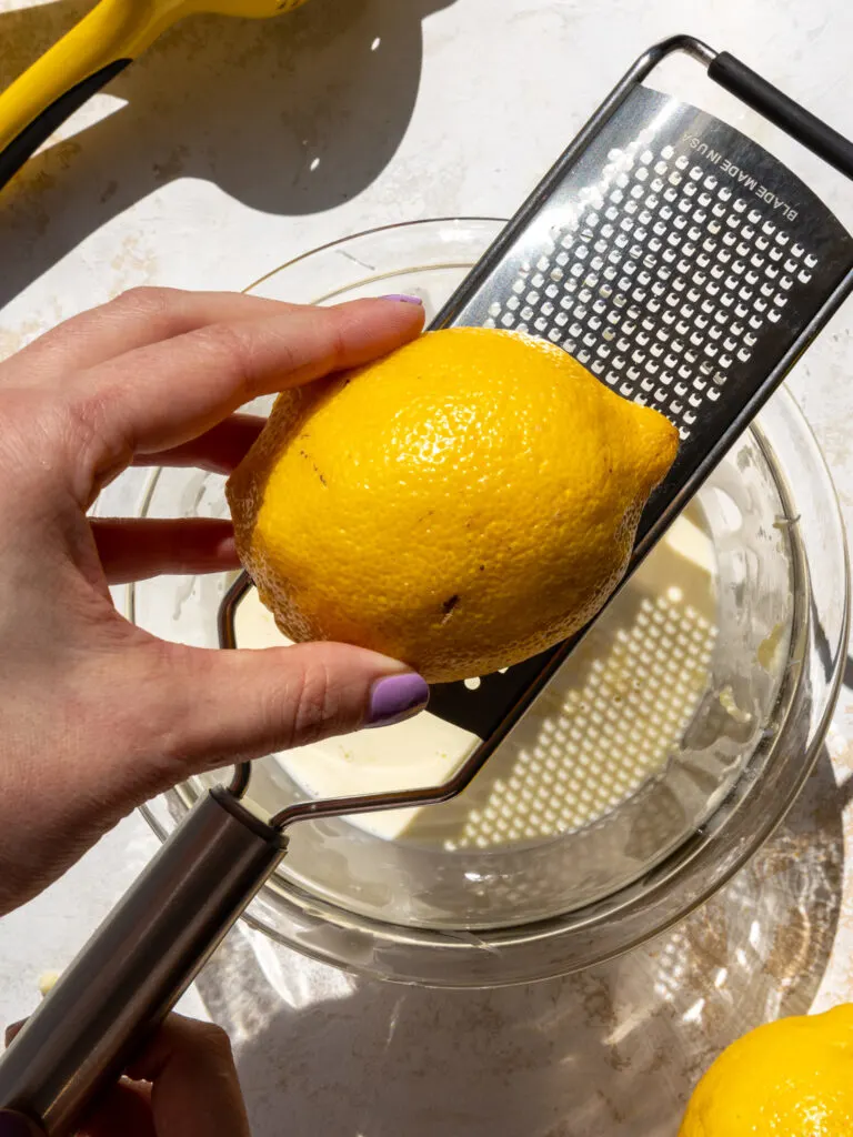 image of a lemon being zested into white chocolate ganache with a microplane grater