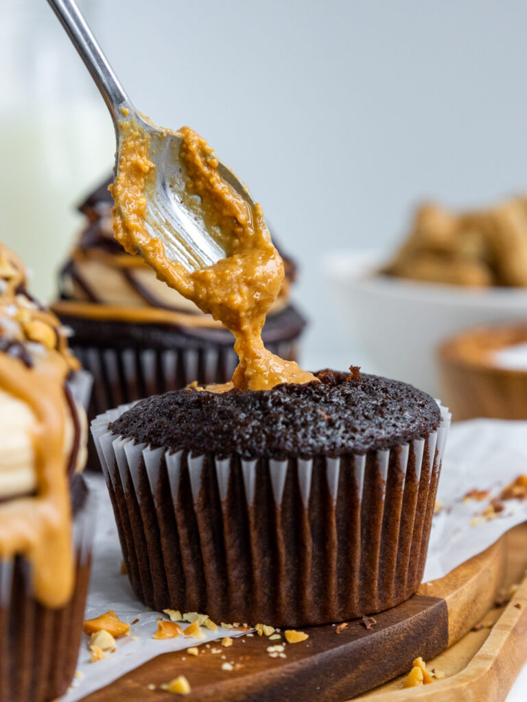 image of peanut butter being spooned into the center of a chocolate cupcake