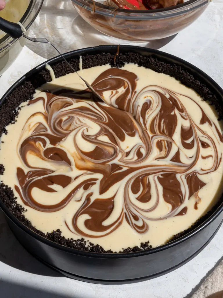 image of vanilla and chocolate cheesecake batter being swirled together to make a marbled cheesecake