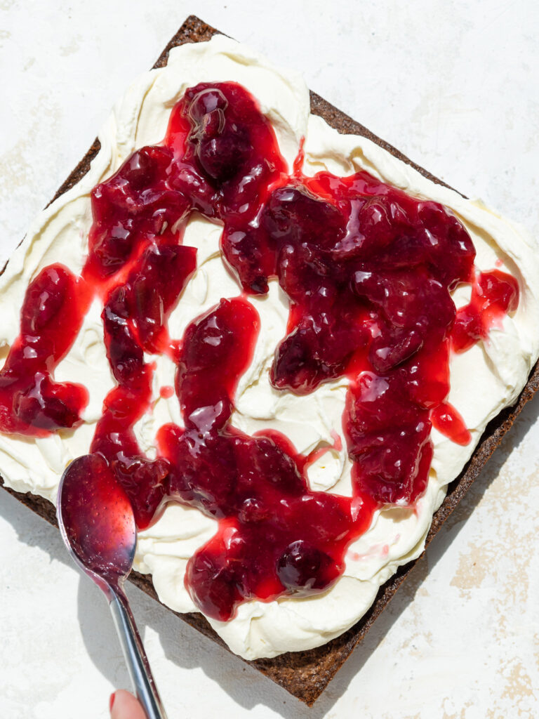 image of cherry kirsch topping being spooned on top of whipped cream to make black forest brownies