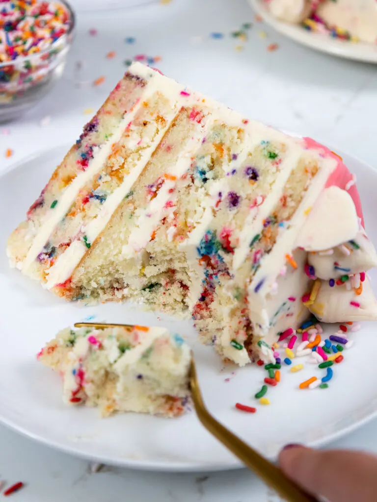 image of a slice of funfetti cake on a plate that's been cut into to show how tender it is