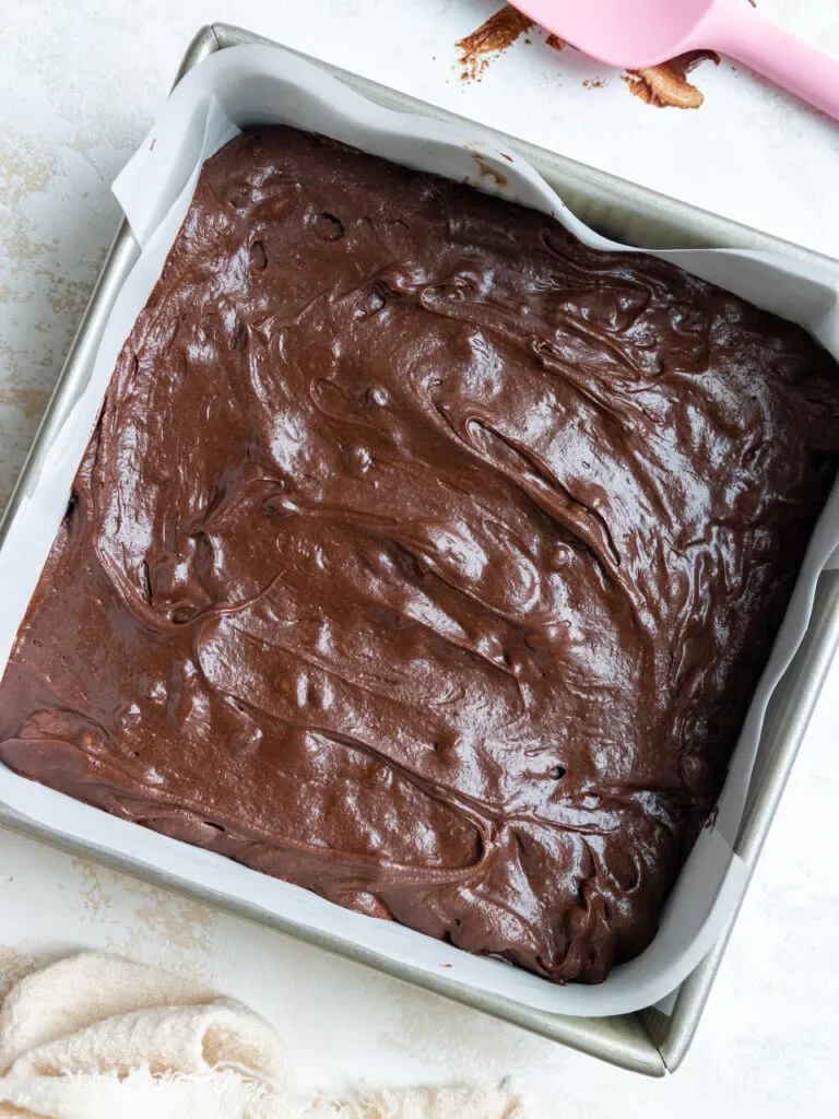 image of dark chocolate brownie batter in a lined square metal pan