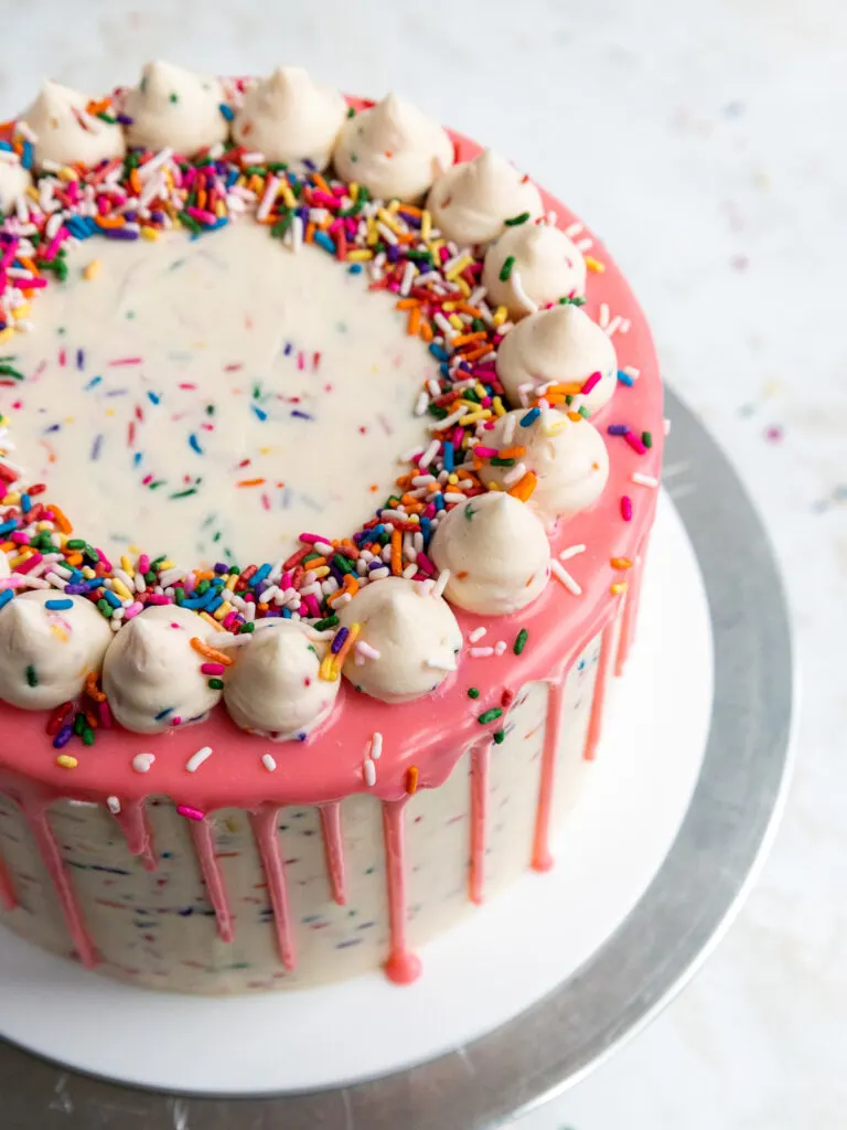 image of a funfetti cake frosted with sprinkle frosting and decorated with a pink ganache drip