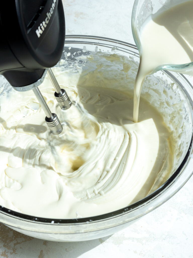 image of heavy cream being poured into a bowl while whipping up stabilized whipped cream with a hand mixer