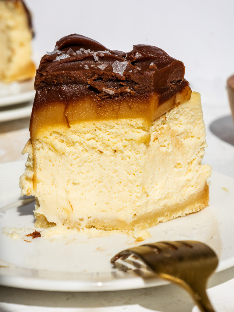image of a slice of millionaire cheesecake that's been cut into to show its decadent layers of caramel and chocolate ganache