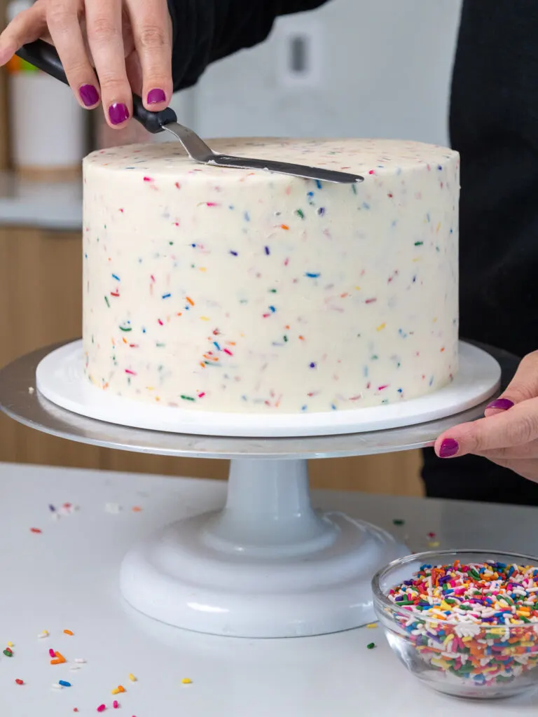 image of sprinkle buttercream being smoothed onto a funfetti cake
