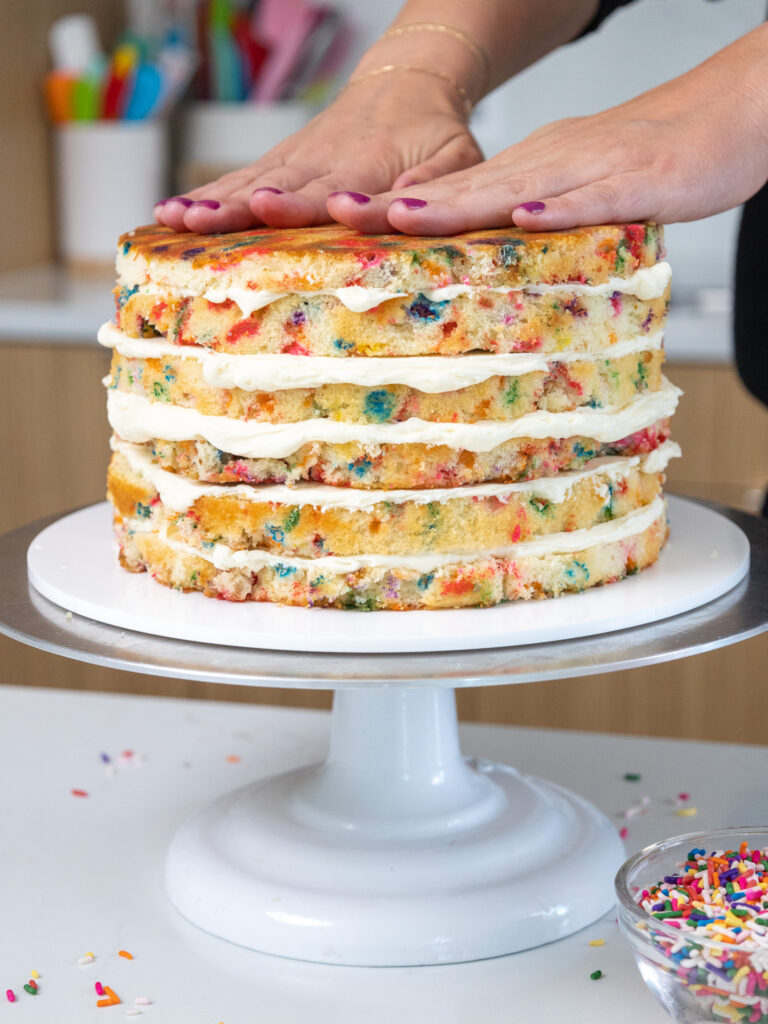 image of funfetti cake layers being frosted and stacked to make a funfetti layer cake