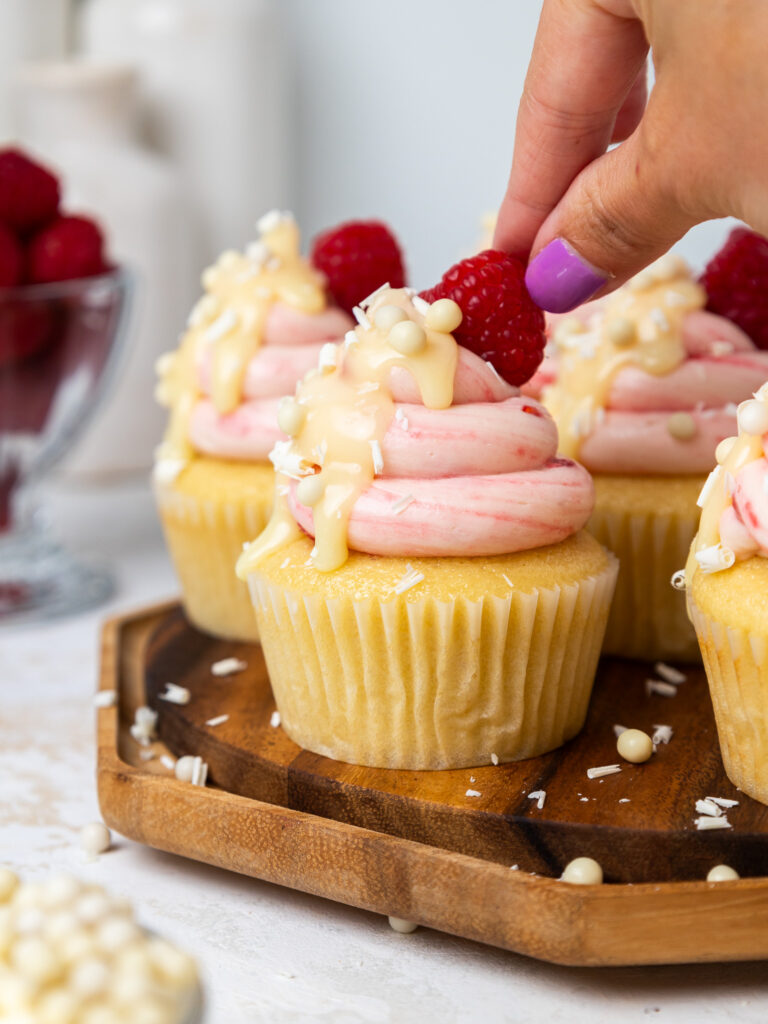 image of a white chocolate raspberry cupcake being garnished with a raspberry