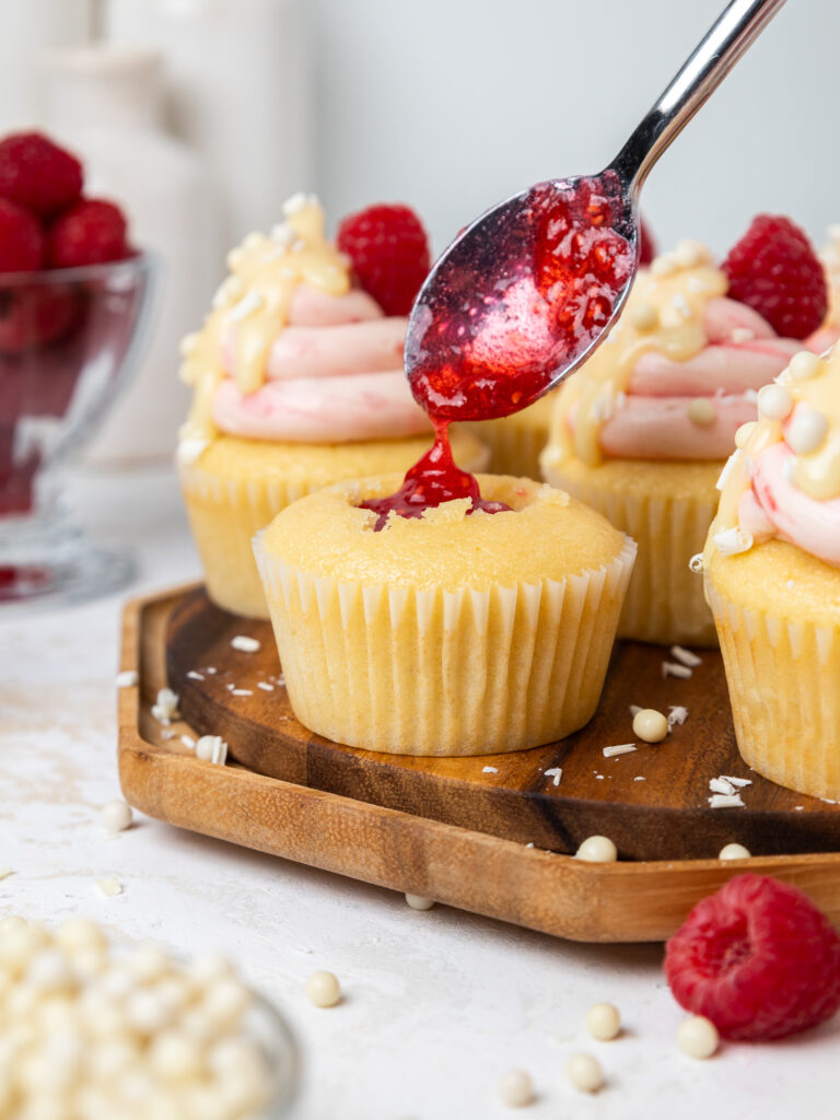 image of white chocolate raspberry cupcakes being filled with raspberry jam