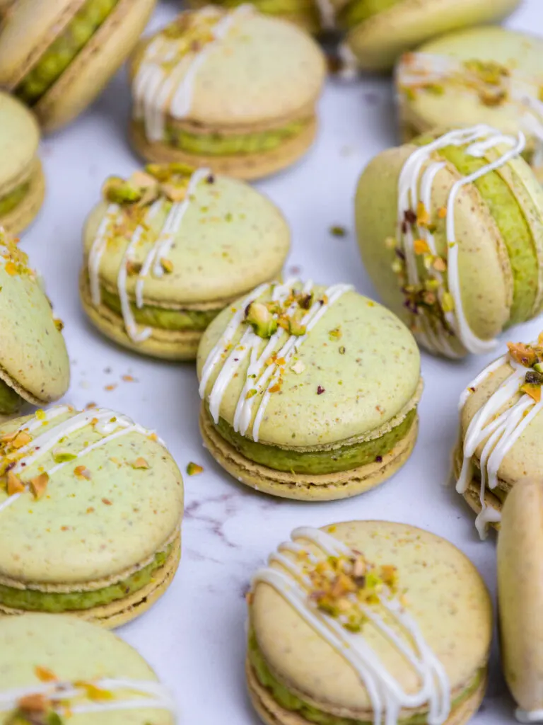 image of pistachio macarons that have been drizzled with white chocolate and topped with chopped pistachios