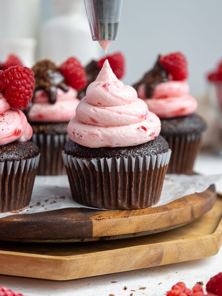 image of a chocolate raspberry cupcake being frosted with raspberry buttercream frosting
