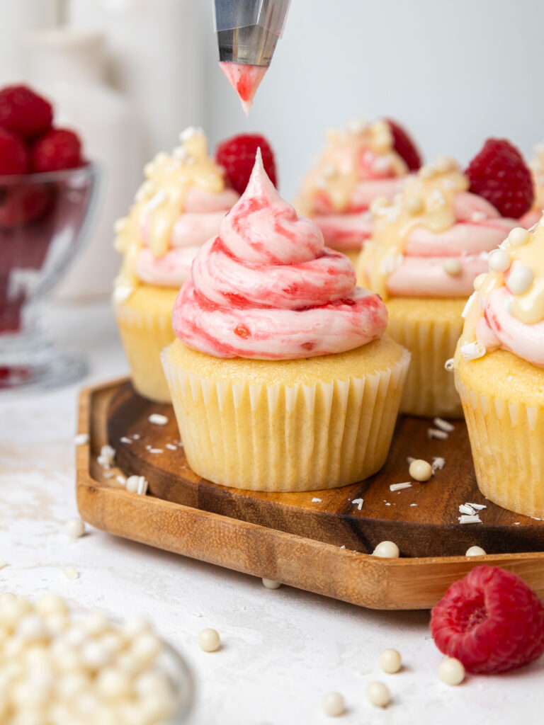 image of a white chocolate raspberry cupcake being frosted with a large swirl of white chocolate raspberry buttercream