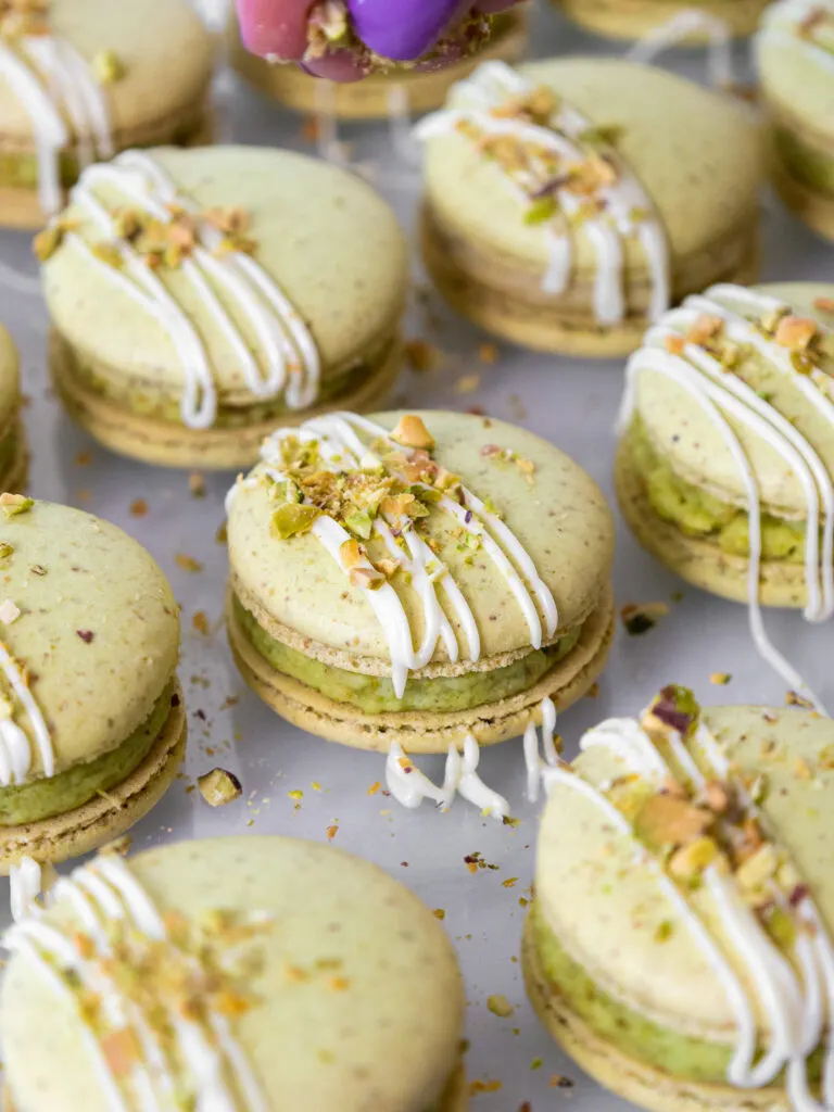 image of pistachio macarons being topped with chopped pistachios and white chocolate