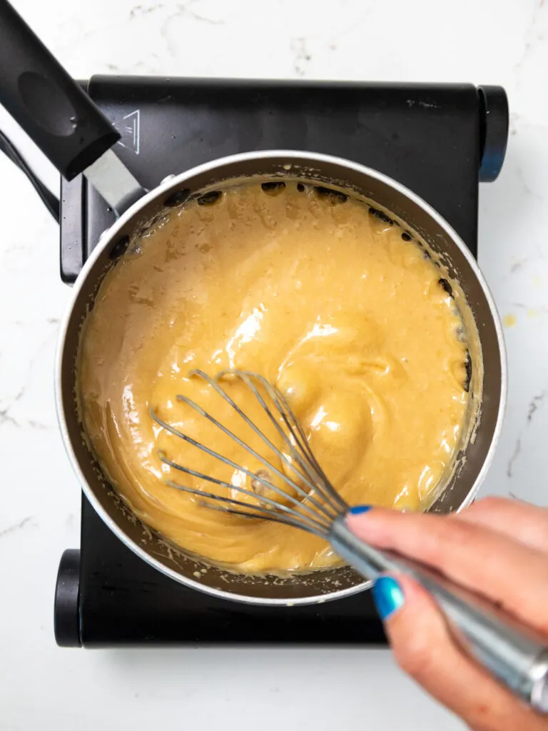 image of thick caramel being cooked down on a stovetop while being stirred with a whisk