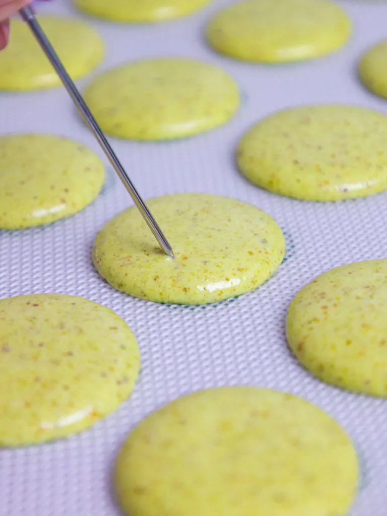 image of bubbles being popped inside macaron shells with a metal scribe