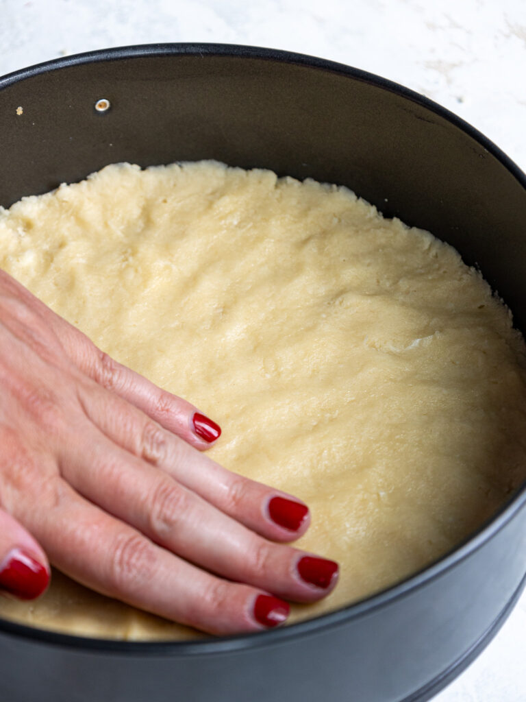 image of shortbread crust being pressed into a cheesecake pan