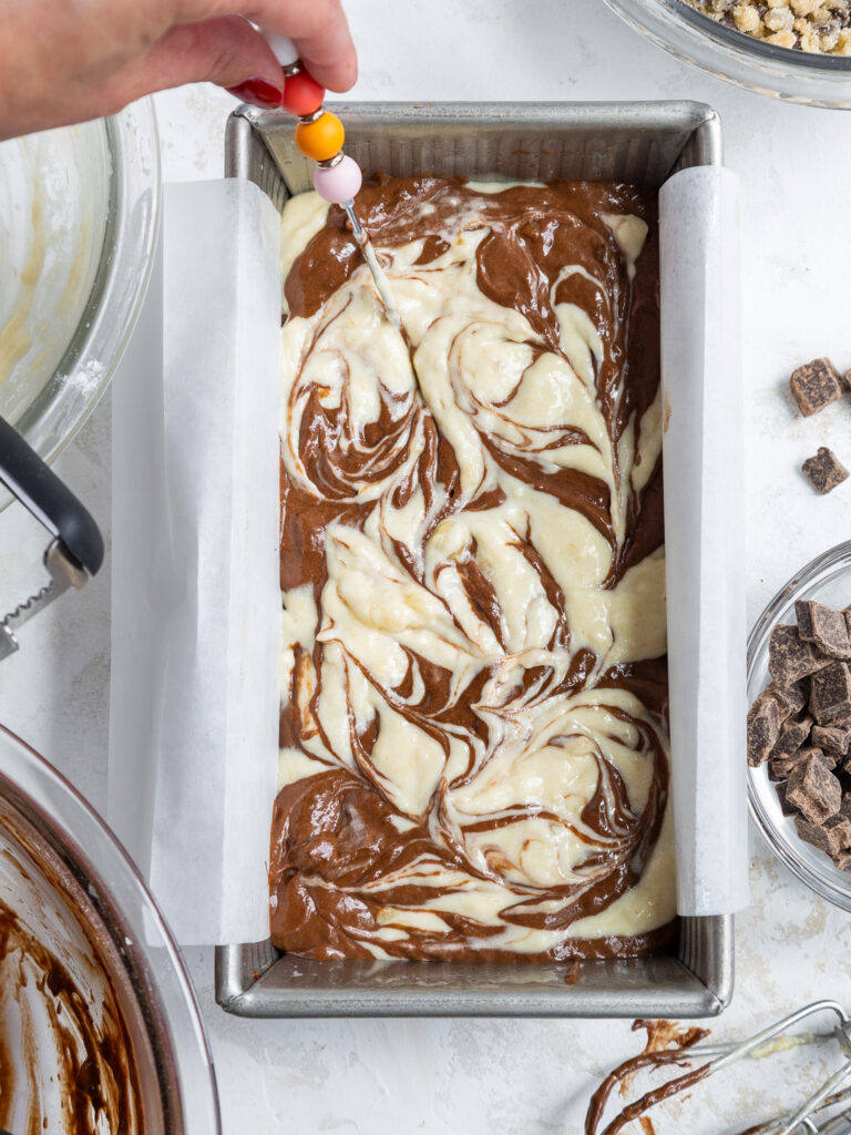 image of marble banana bread batter being swirled together in a metal loaf pan.