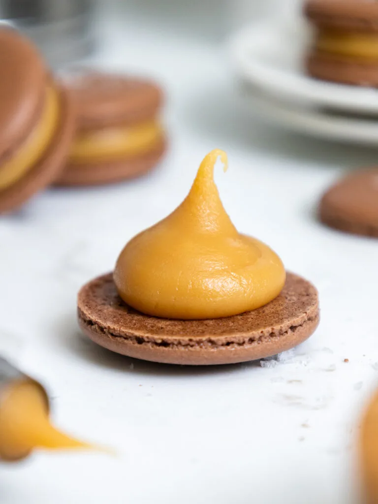 image of thick caramel filling being piped onto a chocolate macaron shell